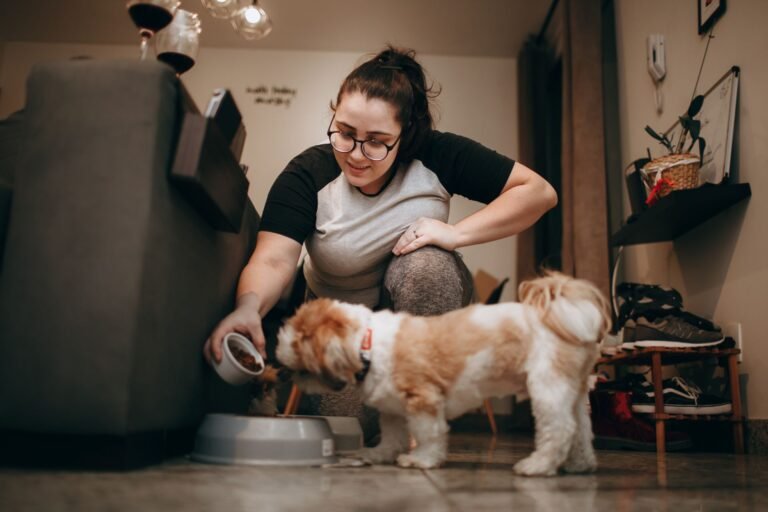 A woman in a casual outfit feeds her small dog indoors