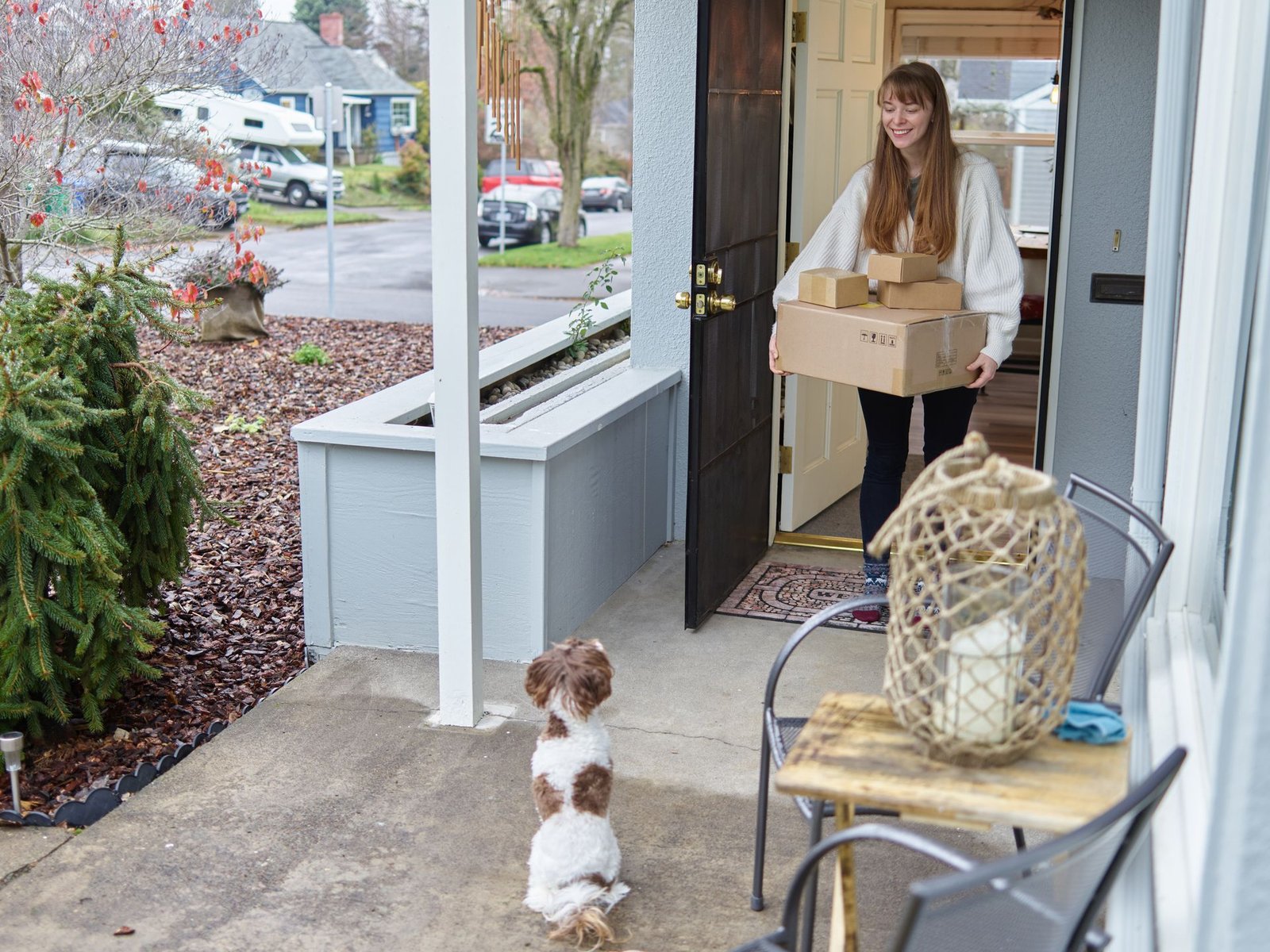 Woman carrying delivery boxes indoors while her dog watches